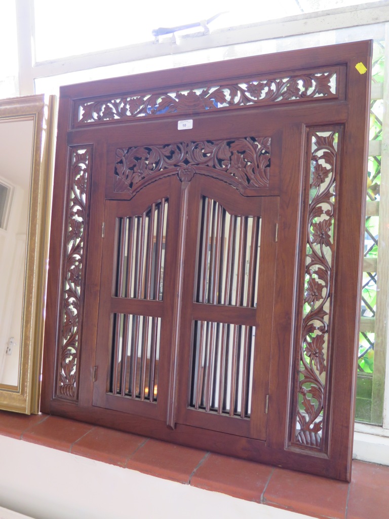 A carved hardwood Indian style wall mirror with pierced foliate carving and two grille doors