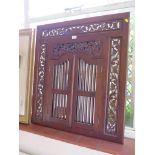 A carved hardwood Indian style wall mirror with pierced foliate carving and two grille doors