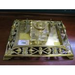 An Edwardian brass ink stand, of rectangular form with pierced border, scroll handles and pen rest