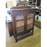 An oak display cabinet, the blind fret carved frieze over lead glazed doors on turned legs joined by