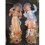 A pair of Bisque figures depicting a boy and a girl with dogs at their feet, 31cm high