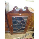 A George III mahogany corner cabinet, the swan neck pediment over a glazed door enclosing shaped