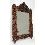 A CONTINENTAL CARVED STAINED PINE WALL MIRROR of scrolling vine design, 85cm x 124cm