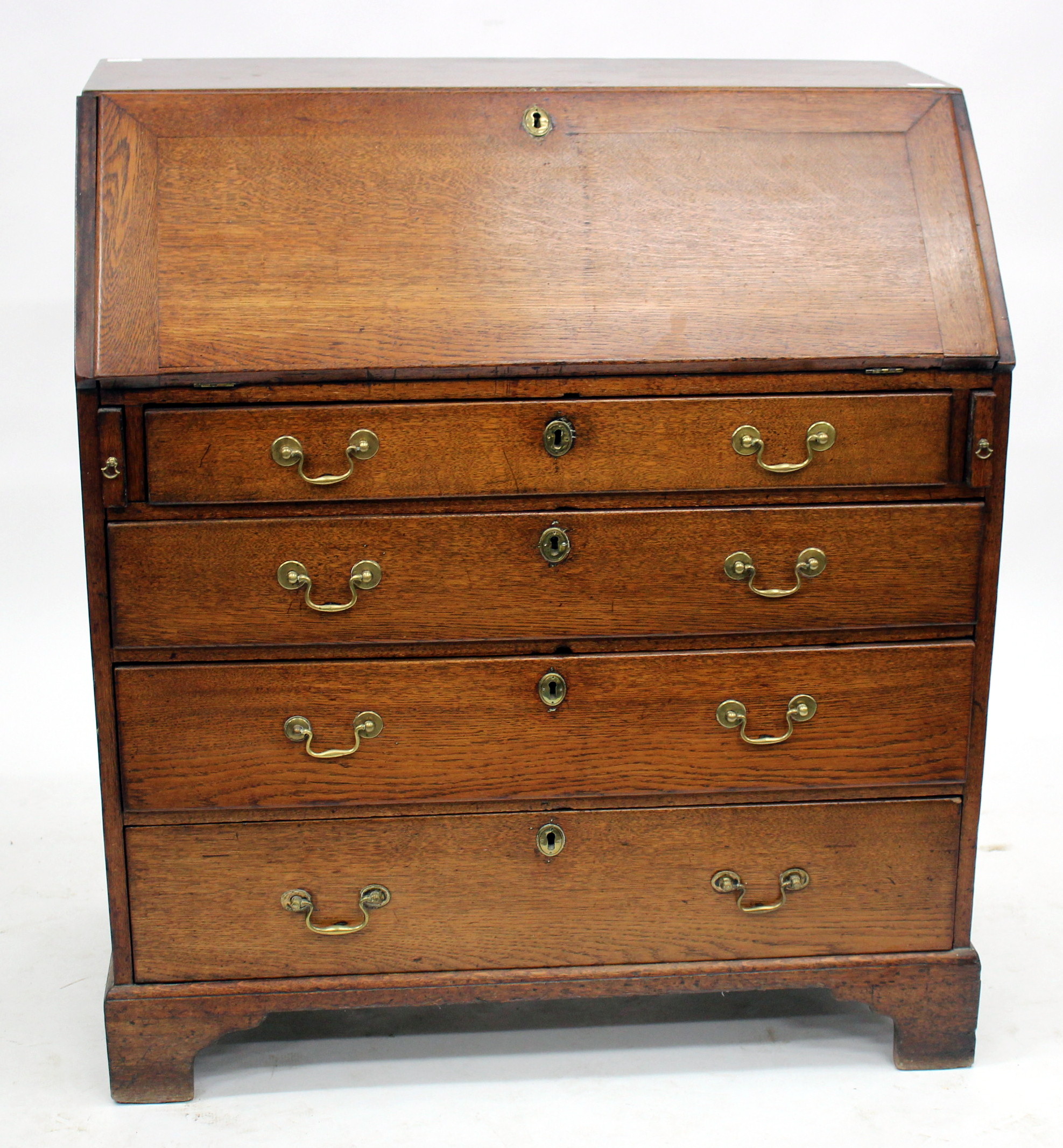 A GEORGE III OAK BUREAU, the fall front opening to reveal pigeon holes and drawers, all above four