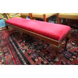 AN OAK LONG LOW STOOL with inset red draylon upholstered cushion and standing on six short