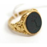 A VICTORIAN GOLD AND BLOOD STONE SET SIGNET RING engraved with a crest of an arm holding a bunch