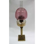 A BRASS CORINTHIAN COLUMN OIL LAMP with a clear glass well and cranberry glass shade 80cm in height