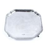 A SQUARE SILVER SALVER with shaped canted corners and gadrooned edge, standing on four shaped