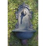 A GREEN PAINTED CAST METAL WALL FOUNTAIN, the decorative back plate with brass tap over a semi