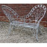 A WHITE PAINTED WROUGHT IRON LOVE SEAT with flower head and scroll decoration, 130cm wide x 102cm