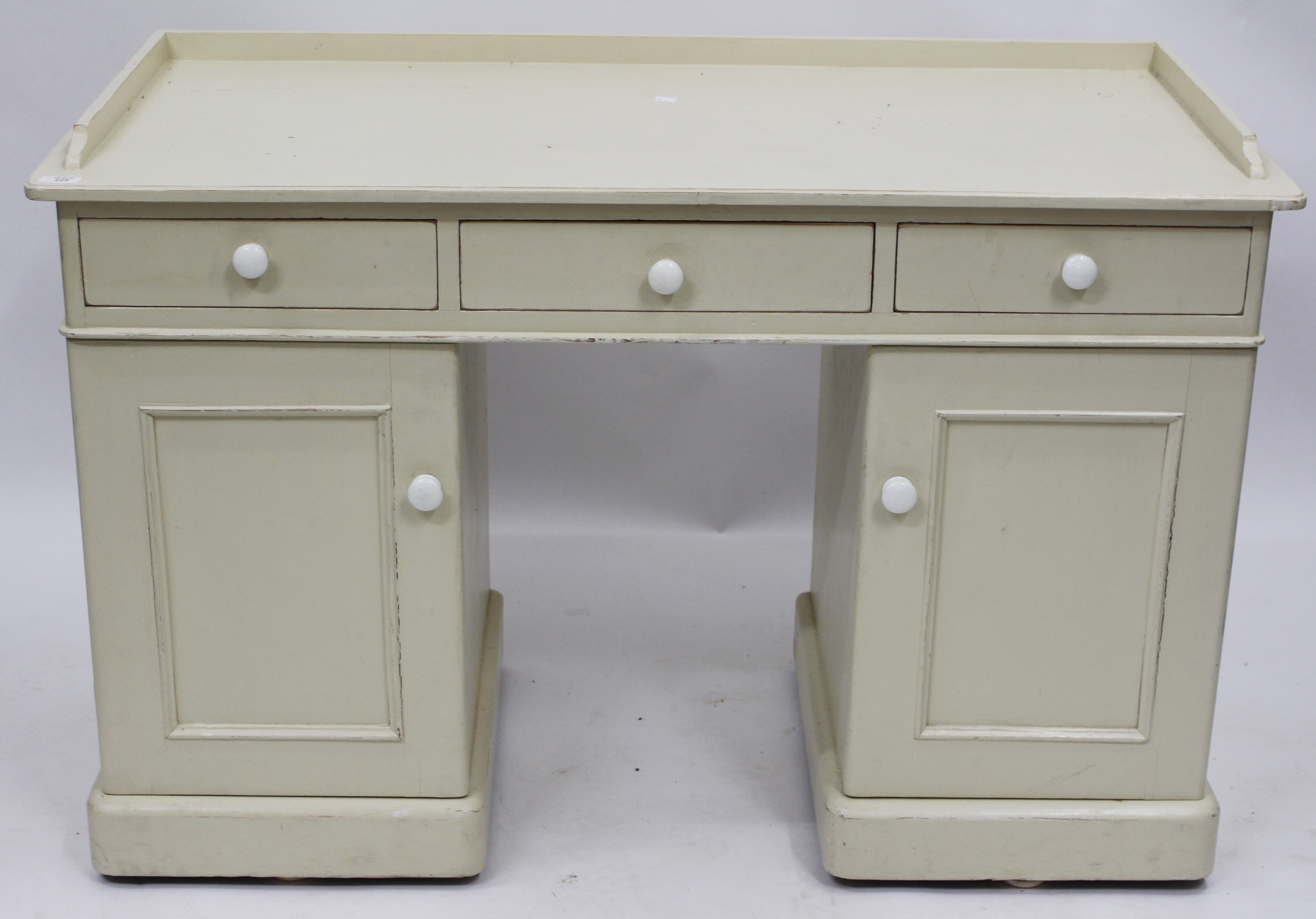 A WHITE PAINTED PINE KNEE HOLE DESK with fielded panel doors, 54cm x 114cm x 77cm