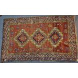 A Kazak rug of red ground, with three central medallions with a centeral flower, surrounded by