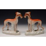 A PAIR OF VICTORIAN STAFFORDSHIRE POTTERY FIGURES of greyhounds, each standing and holding a dead