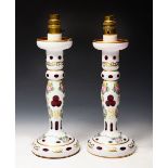 A PAIR OF WHITE OVERLAID CRANBERRY GLASS TABLE LAMPS with faceted, florally painted and gilt