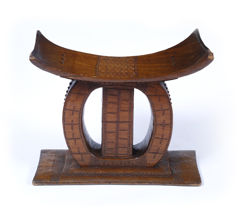 AN ASHANTI WOODEN STOOL of bowed form with stylised geometric decoration on a rectangular plinth,