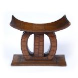 AN ASHANTI WOODEN STOOL of bowed form with stylised geometric decoration on a rectangular plinth,