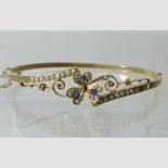 An Edwardian 9 carat gold seed pearl and sapphire set hinged bangle,