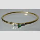 A unmarked hinged bangle, set with a central emerald flanked by diamonds,