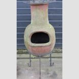 A terracotta chiminea, on a black painted metal stand,