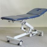A blue padded folding massage table, on an adjustable base,