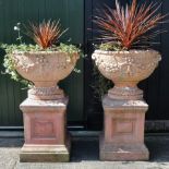 A pair of terracotta urns, on pedestal bases,