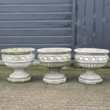 A set of three reconstituted stone planters, on pedestal bases,