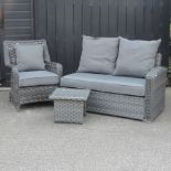 A grey rattan sofa, together with an armchair and a side table,