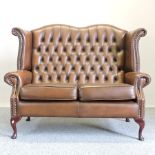 A brown leather upholstered button back wing sofa,