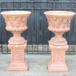 A pair of large red terracotta garden planters, each on a pedestal base,