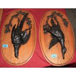 A pair of bronze figures of dead game birds, mounted for wall hanging on oak oval plaques