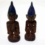 A PAIR OF CARVED IBEJI TWIN FIGURES, male and female. each with purple painted head dress, 10.