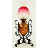 AN ARTS AND CRAFTS EMBOSSED COPPER AND WROUGHT IRON OIL LAMP, THE SHADED CRANBERRY GLASS TULIP