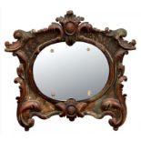 A NORTH ITALIAN CARVED WOOD MIRROR, THE BEVELLED OVAL PLATE SECURED BY FOUR MOULDED GLASS NUTS, 44CM