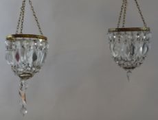 A pair of hanging chandeliers with glass drops suspended from a gilt metal rim,