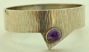 An amethyst set bangle, the cabochon off set to a textured 1.