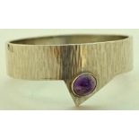 An amethyst set bangle, the cabochon off set to a textured 1.