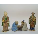 Three Chinese  mudman models, of two figures playing chess, 13cm wide, a wiseman holding a fruit,