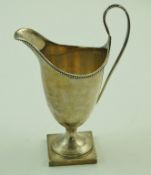 A silver helmet shaped cream jug with a beaded border, a loop handle and a square foot,