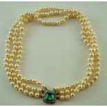 A uniform three row cultured pearl necklace with an emerald and diamond set clasp,