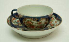 A Worcester tea bowl and saucer with kakiemon flowers within gilt reserves on a blue scale ground,