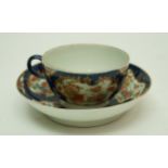 A Worcester tea bowl and saucer with kakiemon flowers within gilt reserves on a blue scale ground,