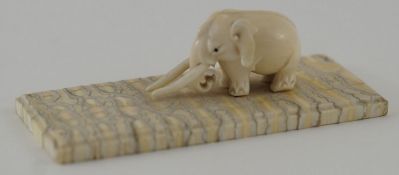 An early 20th century carved ivory figure of an elephant on a rectangular fossilized mammoth tusk
