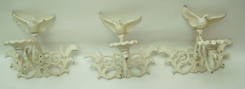 A set of three cast metal wall brackets each with a candle sconce surmounted with a bird,