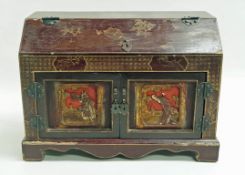 A Chinese lacquered table cabinet with sloping hinged top above two doors with inset carved temple