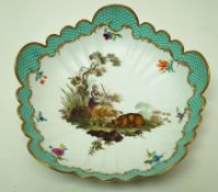 A Meissen lobed round dish painted in enamels with a shepherdess and her sheep with turquoise brick