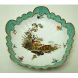 A Meissen lobed round dish painted in enamels with a shepherdess and her sheep with turquoise brick