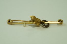 A 15ct gold kitten bar brooch, the young cat playing with a pearl (untested and unwarranted) 'ball',