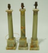 A set of three onyx and gilt metal table lamps, each in the form of a column on square bases,