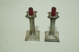 A pair of silver plated candlesticks in the form of a Corinthian column on a stepped base.