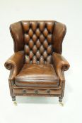 A leather wing back armchair with button back and turned legs on brass casters